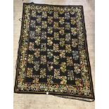 A needlepoint rug, the black field worked in a floral design and bordered 212cm x 304cm