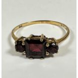 A 9ct gold three stone garnet ring the centre cushion cut garnet approximately 0.3ct, flanked by a