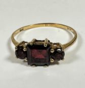 A 9ct gold three stone garnet ring the centre cushion cut garnet approximately 0.3ct, flanked by a