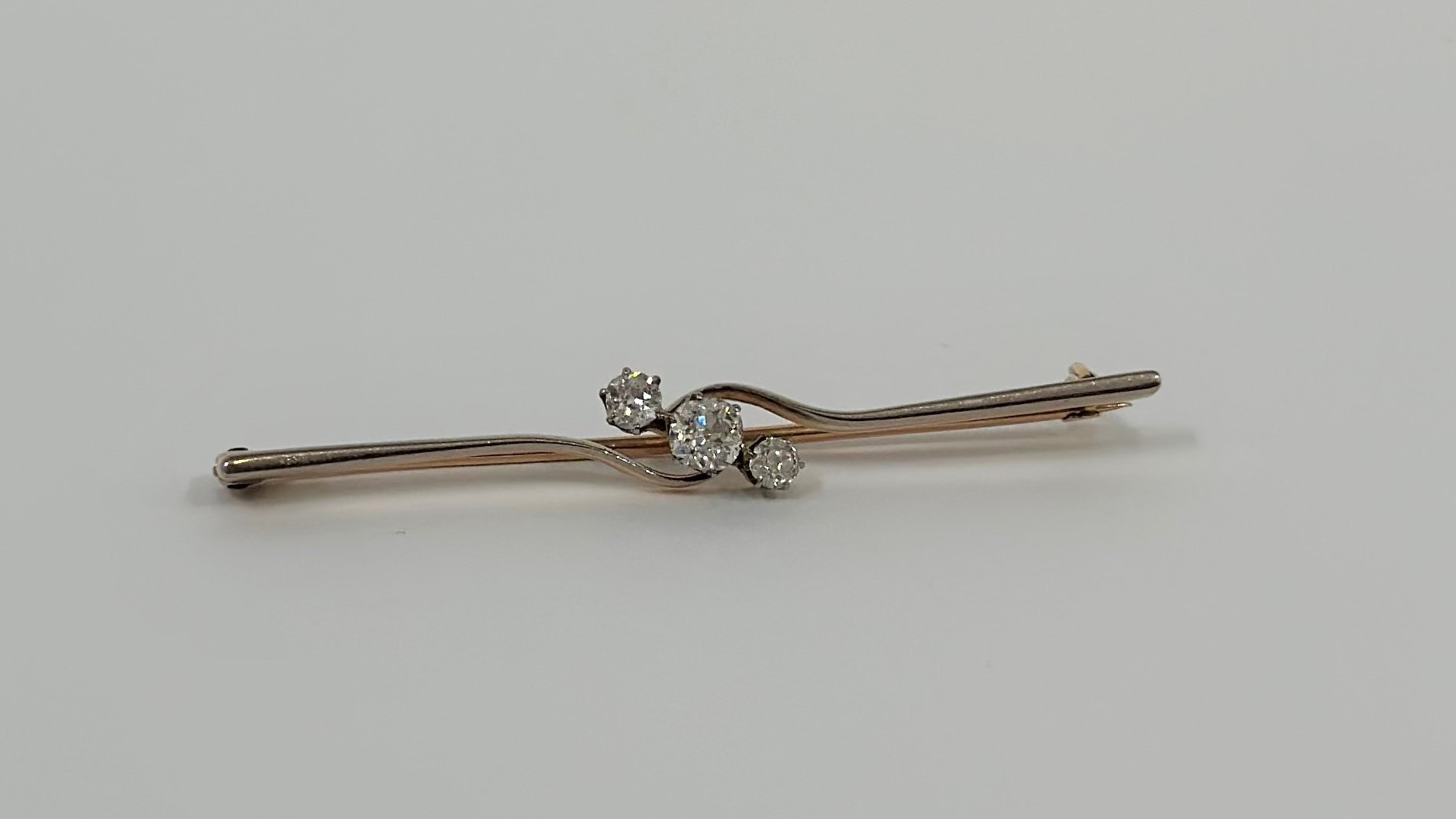 A three-stone diamond bar brooch, the three graduated round brilliant-cut stones crossover set on an