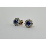 A pair of sapphire and diamond stud earrings, each with round-cut sapphire claw-set within a band of