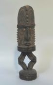 A carved wooden standing figure, Papua New Guinea, with cowrie shell eyes, elaborate headdress and