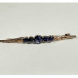 A yellow metal bar brooch set five coloured sapphires, mounted in claw setting, the centre