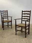 A pair of stained oak ladder back carver dining chairs, 20th century, with string seat, raised on