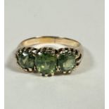 A yellow metal graduated three stone peridot ring, the centre oval cut stone (0.75ct), flanked by