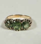 A yellow metal graduated three stone peridot ring, the centre oval cut stone (0.75ct), flanked by