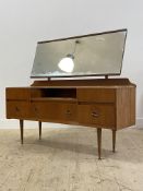 A mid century teak dressing table, the rectangular swing mirror over five drawers, raised on