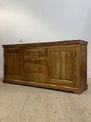 A Mango wood sideboard, fitted with four centre drawers, flanked by two panelled cupboards, raised