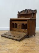 A Victorian oak table secretaire, the raised back with floral carved pediment centred by a