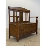 An Arts and Crafts period oak hall bench, the shaped crest rail over slatted back with inlay to