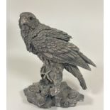 A hallmarked silver (resin filled) figure of a falcon with inset glass eyes perched on a rocky outcr