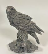 A hallmarked silver (resin filled) figure of a falcon with inset glass eyes perched on a rocky outcr