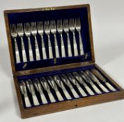 An Edwardian oak canteen containing a set of twelve mother of pearl handled Epns knives and a set of