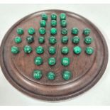 A dark stained oak circular solitaire board with set of malachite balls- one ball replaced with