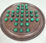 A dark stained oak circular solitaire board with set of malachite balls- one ball replaced with