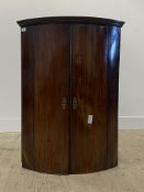 A Georgian mahogany bow front wall hanging corner cabinet, with two doors enclosing shelves H92cm,