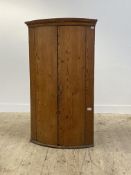 A large pitch pine bow front wall hanging corner cupboard, 19th century, with dentil cornice and two