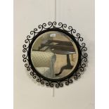 A wrought metal circular wall hanging mirror, the frame with conforming C scrolls enclosing a