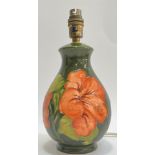 A Moorcroft pottery 'Hibiscus' lamp decorated with red tube lined flowers on a green ground (
