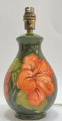 A Moorcroft pottery 'Hibiscus' lamp decorated with red tube lined flowers on a green ground (