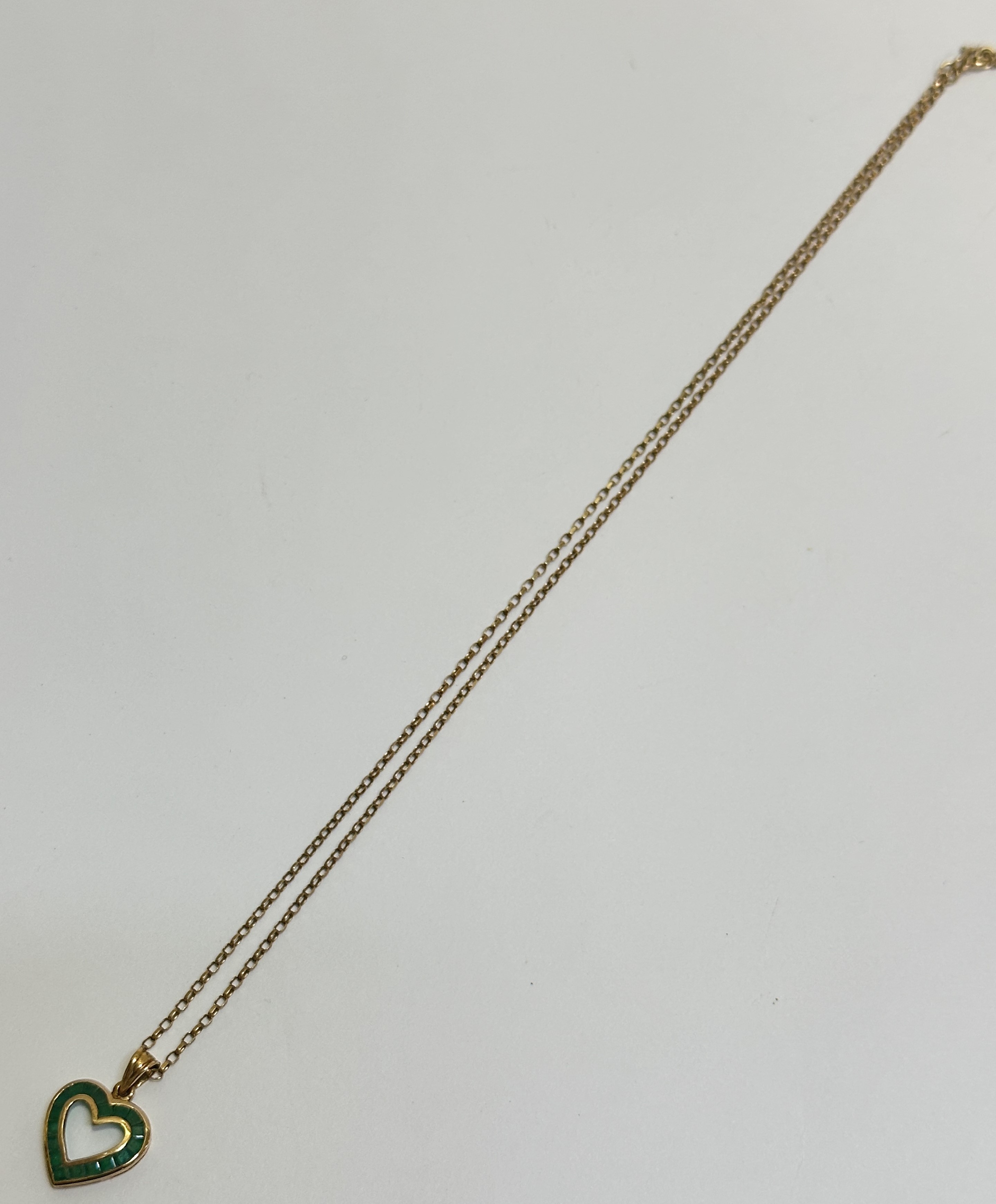 A 9ct gold open work heart shaped pendant set eighteen calibre set emeralds mounted on trace link