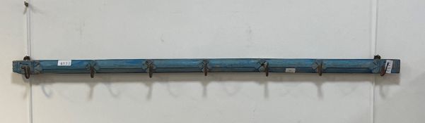 A rustic blue painted hardwood wall hanging bracket fitted with seven wrought iron coat hooks