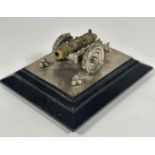 A miniature brass table cannon on chrome carriage mounted on crome plaque and stepped ebonised base,