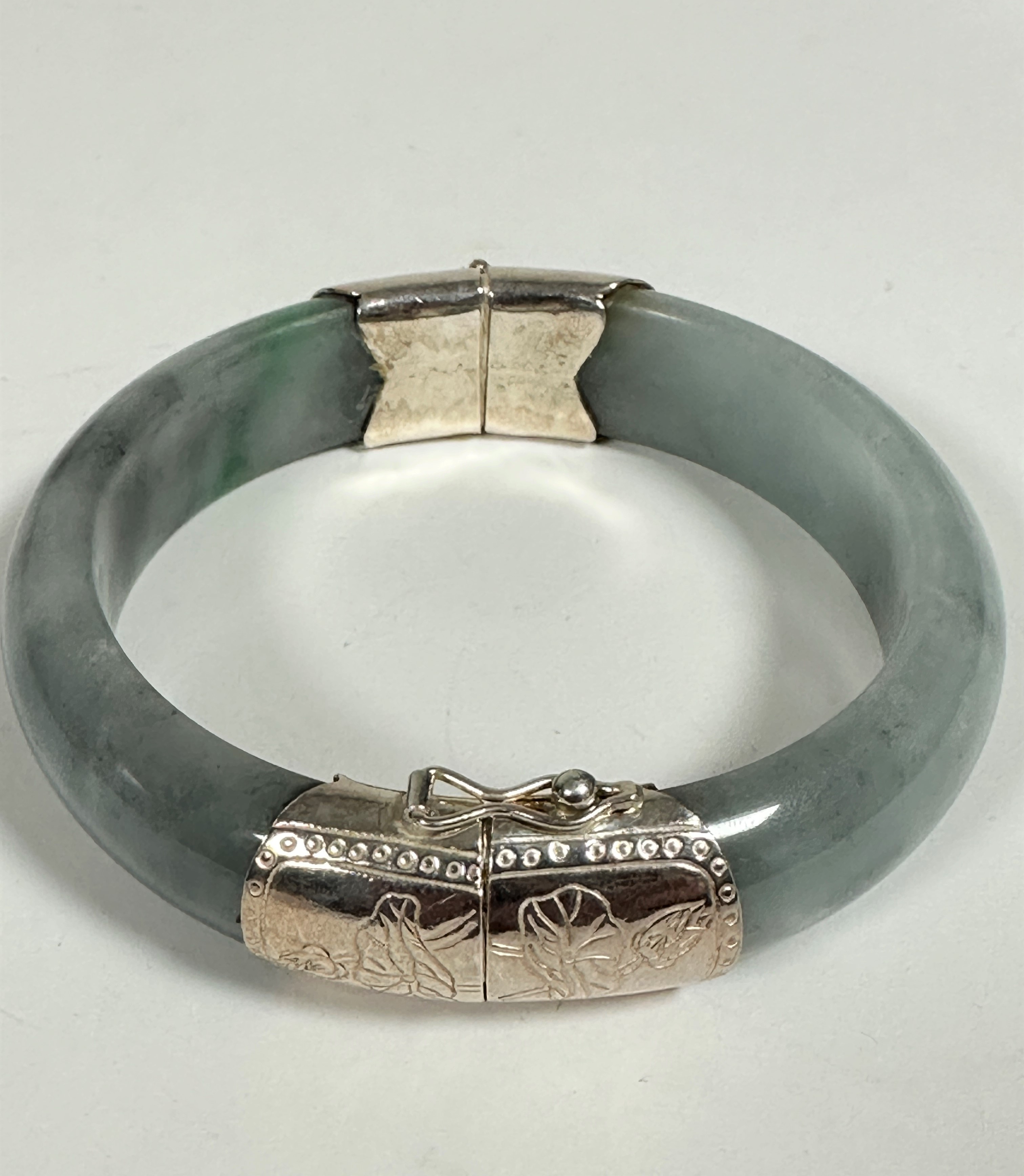 A Chinese white metal mounted circular grey/ celedon coloured Jadite bangle with engraved water lily