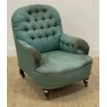 An early 20th century armchair, upholstered in buttoned teal damask, raised on turned supports and