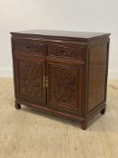 A Chinese hardwood side cabinet, with panelled top over two drawers and two carved panel doors,