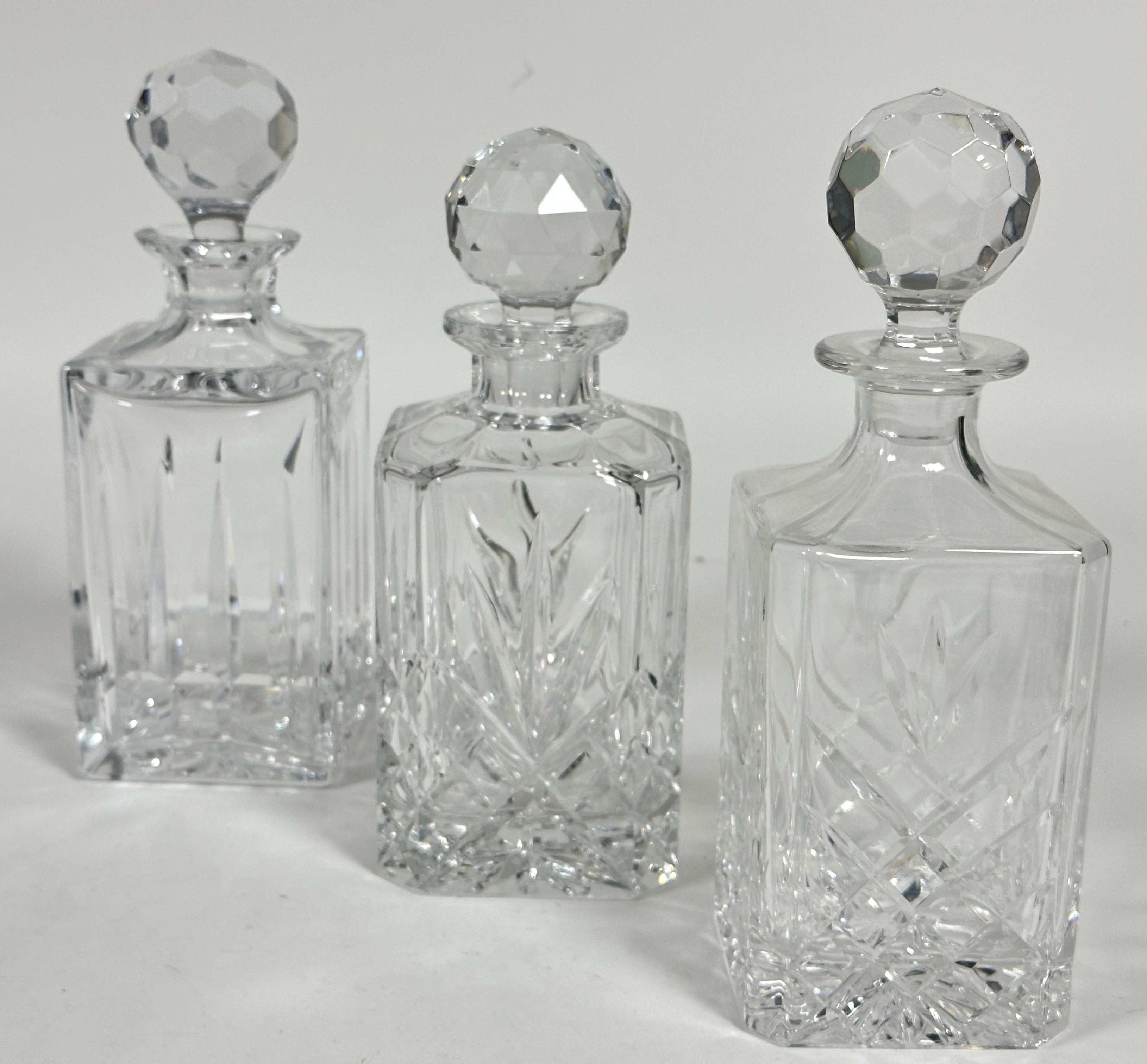 A group of three crystal square cut Whisky decanters with faceted ball pattern stoppers.( 2 x H 26cm