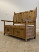 A pine hall bench, the four panel back above open arms and two drawers to base, raised on stile