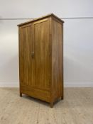 A Contemporary oak wardrobe, the twin panelled doors opening to an interior fitted for hanging,