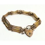 A yellow metal gate link bracelet with 9ct gold engraved heart shaped padlock and safety chain, (