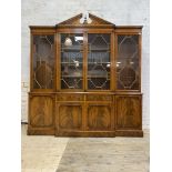 A Georgian style mahogany breakfront bookcase, the broken arch pediment with urn finial over