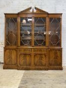 A Georgian style mahogany breakfront bookcase, the broken arch pediment with urn finial over