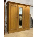 A 19th century pine triple wardrobe, the projecting cornice over two panelled doors flanking a