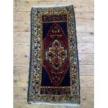 A small hand knotted Persian style rug, the dark field with geometric medallion and bordered 103cm x