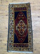 A small hand knotted Persian style rug, the dark field with geometric medallion and bordered 103cm x
