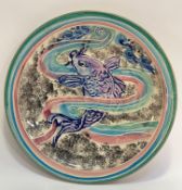 A decorative charger decorated with purple, pink, blue, black and green glazing with koi fish to