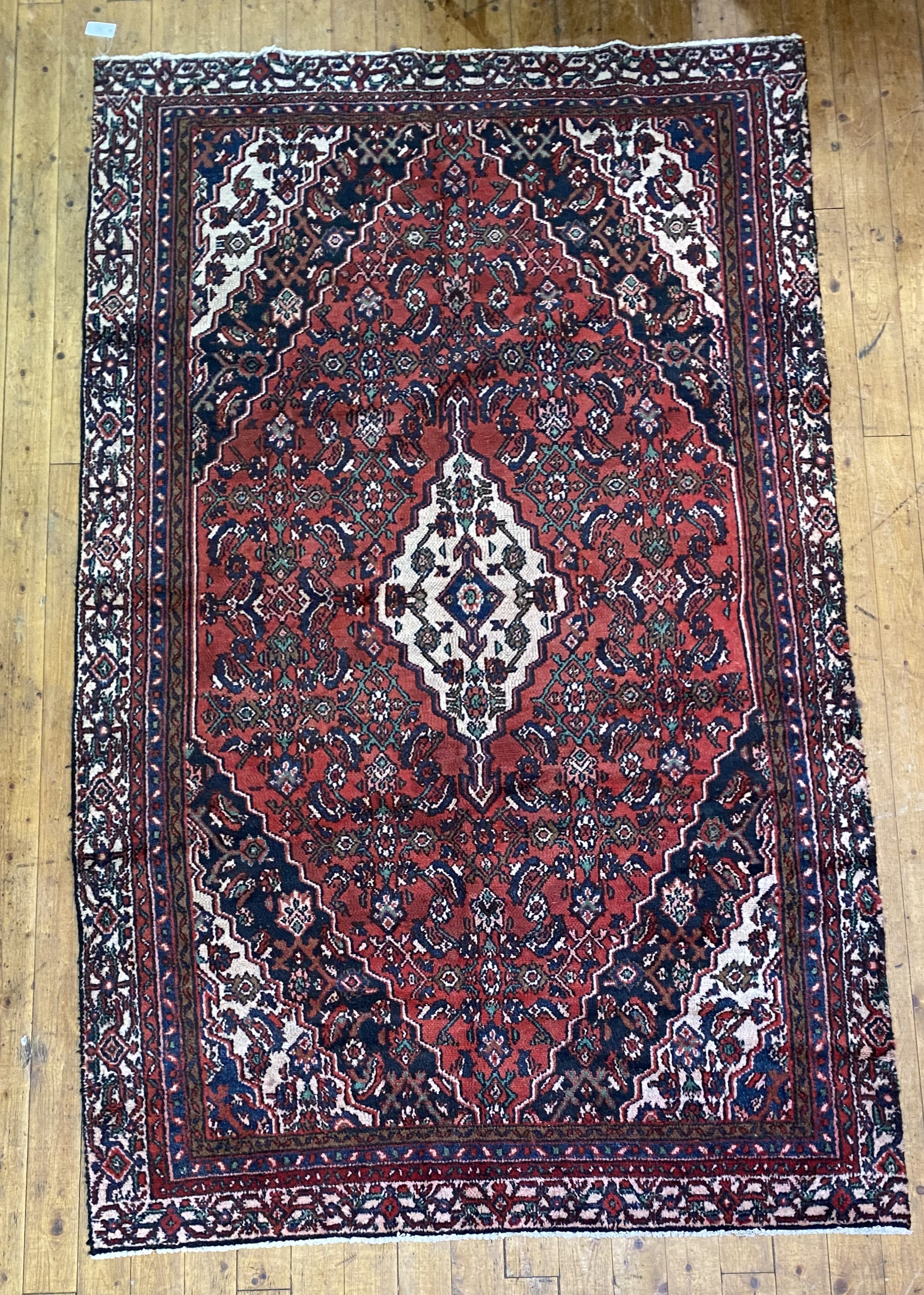 A hand knotted Persian rug, the busy red ground with ivory medallion and spandrels within a