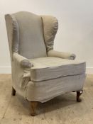 An early 20th century wing back chair, with later fitted natural cotton cover, raised on stained oak