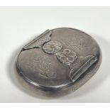 A white metal vesta case, c. 1900, probably Japanese, of shaped oval form, the cover with mixed