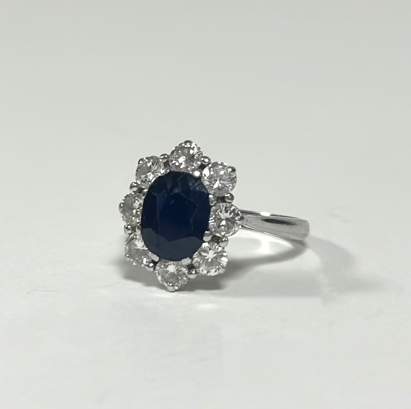 A sapphire and diamond cluster ring the oval-cut sapphire weighing c. 2ct, claw-set within a band of