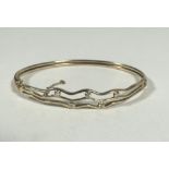 A yellow metal triple wave stiff hinged bangle five Diamonds in rub over setting and safety chain