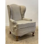 An early 20th century wing back chair, with later fitted natural cotton cover, raised on stained oak