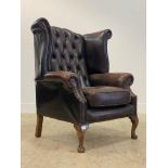 A Georgian style wing back armchair, upholstered in deep buttoned tan leather, raised on cabriole