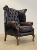 A Georgian style wing back armchair, upholstered in deep buttoned tan leather, raised on cabriole
