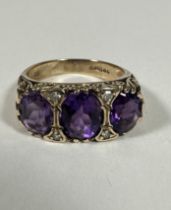A 9ct Gold graduated three stone Amethyst and Diamond ring, the oval centre stone set with four