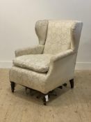 A late Victorian wing back chair, upholstered in ivory damask, raised on turned front supports